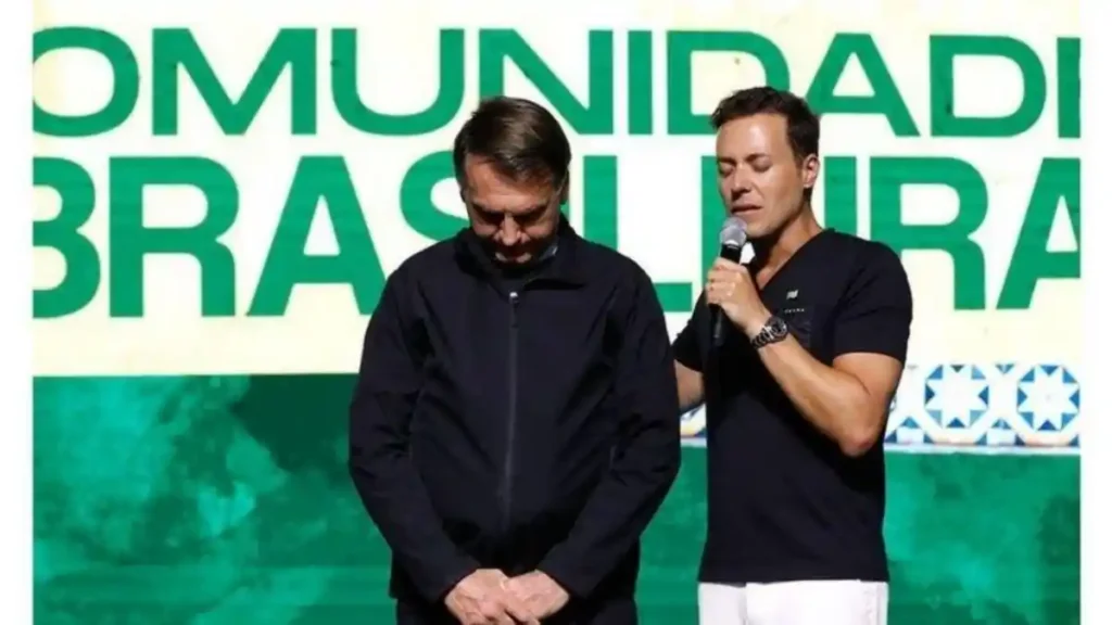 andre valadao ora ao lado de jair bolsonaro em evento com painel verde ao fundo