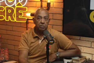 William Lourenço Braga durante participação em podcast, sentado em estúdio com parede de tijolos, falando ao microfone.