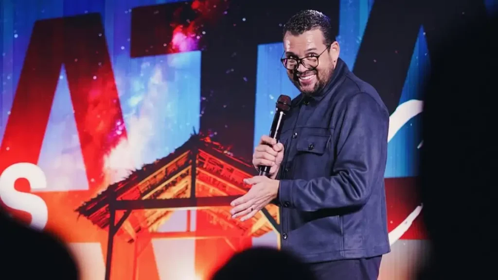 Pastor Jackson Antonio, da Catedral Internacional, segura um microfone e sorri no palco durante evento com telão colorido ao fundo