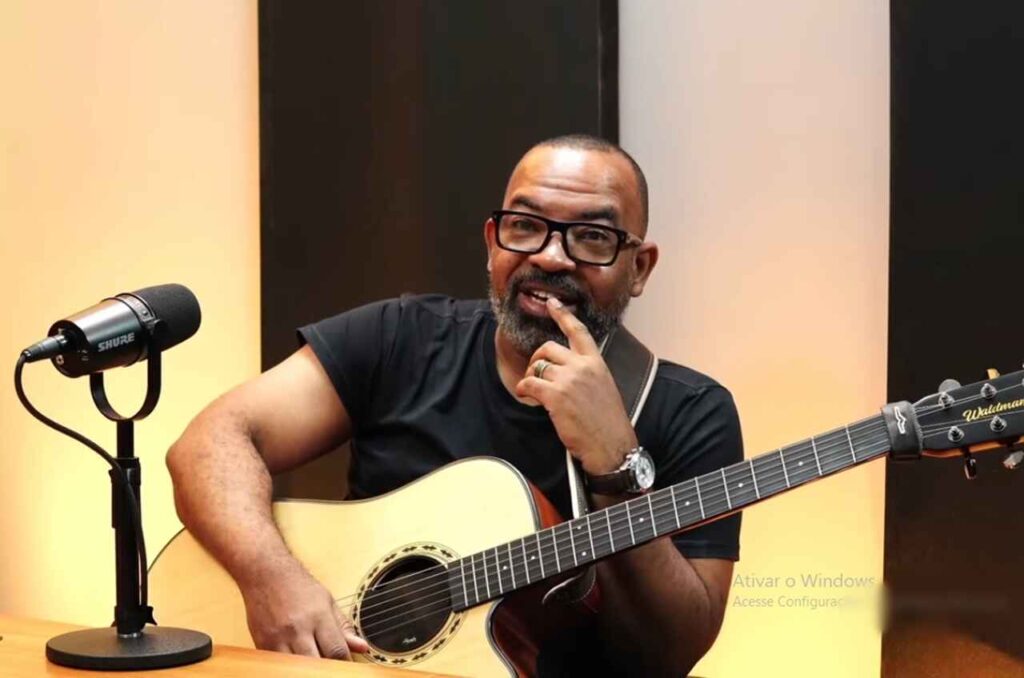 Cantor Luiz Arcanjo com violão durante participação em estúdio ao lado de microfone.