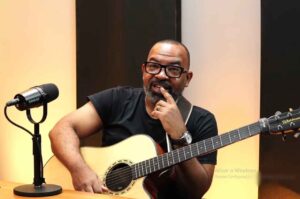 Cantor Luiz Arcanjo com violão durante participação em estúdio ao lado de microfone.