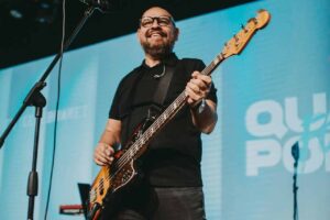 Marcus Salles toca baixo e canta durante apresentação em culto gospel com telão ao fundo.