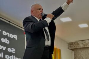 Pastor Ezequias Silva pregando ao microfone com a mão levantada durante culto.