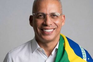 Pastor Junior Trovão sorrindo em retrato com a bandeira do Brasil