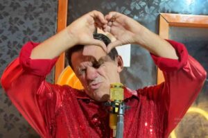 Vocalista da banda Xote Santo cantando ao microfone enquanto faz gesto de coração com as mãos durante apresentação.