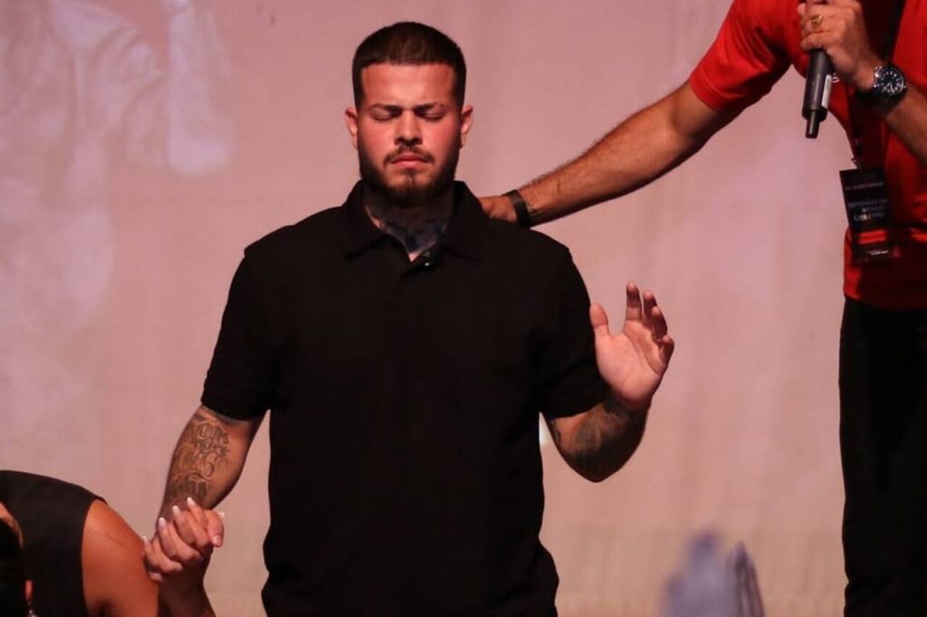 Cantor Jottapê em momento de oração no palco, de olhos fechados