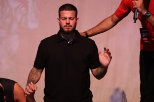 Cantor Jottapê em momento de oração no palco, de olhos fechados