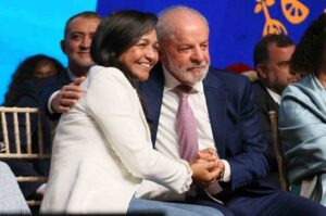 Eliziane Gama e Lula sentados lado a lado, de mãos dadas, durante evento público.