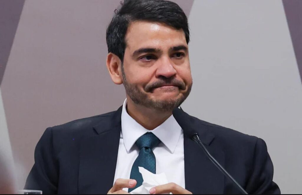 Jorge Messias em coletiva, segurando papel e com expressão séria durante pronunciamento.