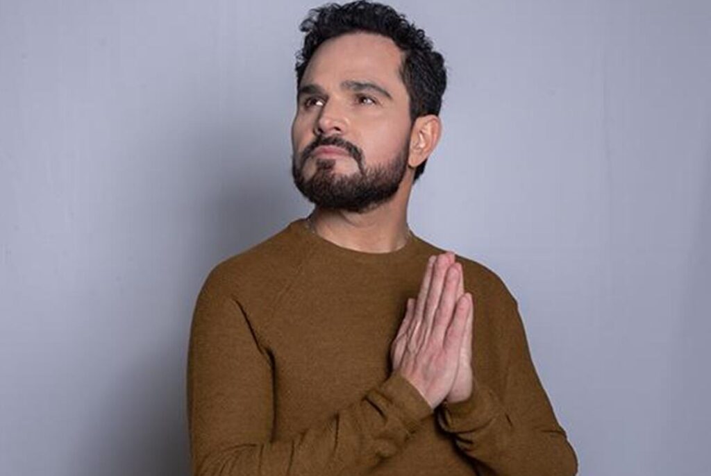 Luciano Camargo em pose de oração, com mãos unidas e olhar voltado para cima.