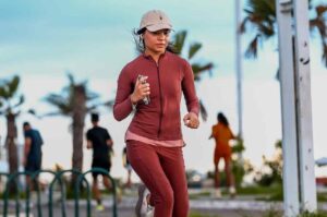 Cantora gospel Maria Marçal praticando corrida ao ar livre, usando roupa esportiva.