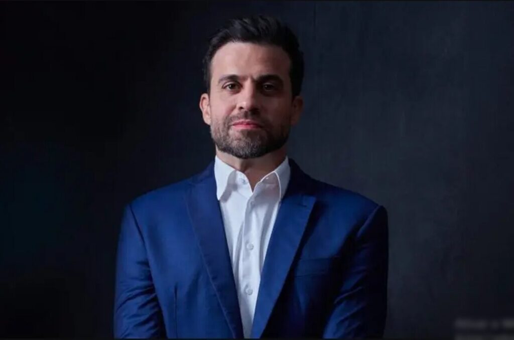 Pablo Marçal em retrato formal, vestindo terno azul e camisa branca, com expressão séria.