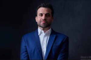 Pablo Marçal em retrato formal, vestindo terno azul e camisa branca, com expressão séria.