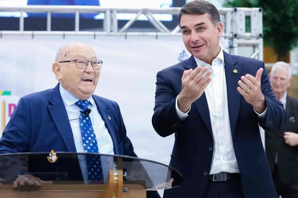 Pastor José Wellington e Flávio Bolsonaro durante evento público, ao lado de púlpito