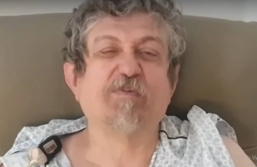 Pastor Luiz Sayão aparece deitado em leito hospitalar, usando vestimenta médica.