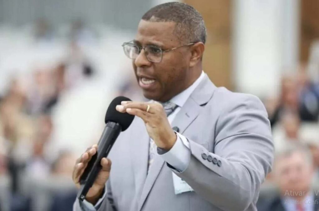 Pastor Osiel Gomes pregando com microfone em evento religioso, usando terno cinza.