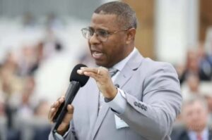 Pastor Osiel Gomes pregando com microfone em evento religioso, usando terno cinza.