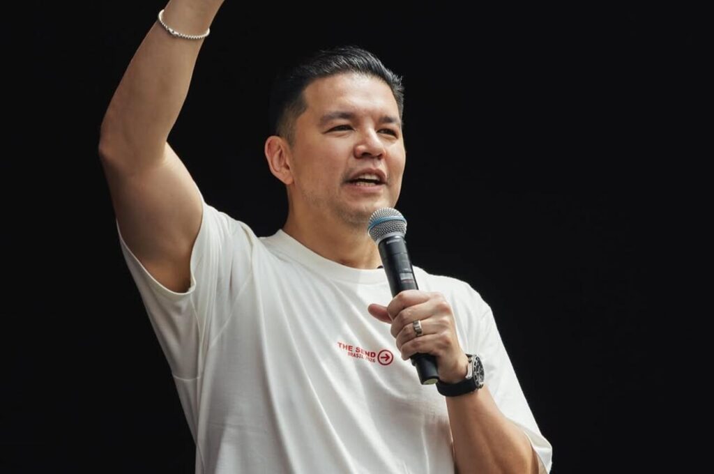 Pastor Téo Hayashi pregando com microfone em mãos, levantando o braço durante ministração