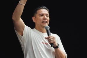 Pastor Téo Hayashi pregando com microfone em mãos, levantando o braço durante ministração