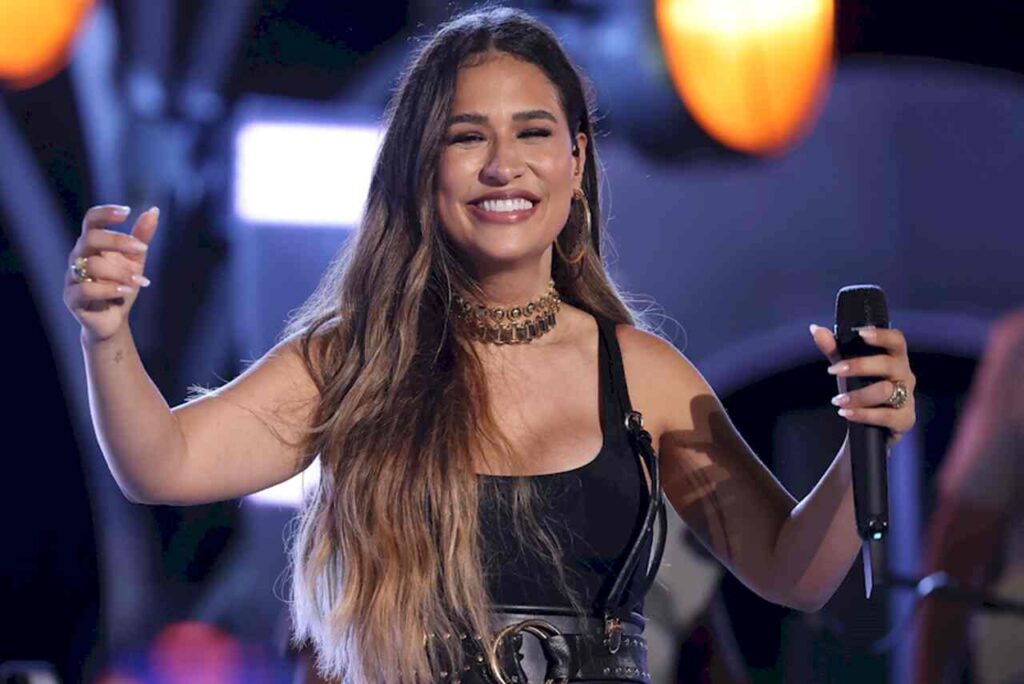 Cantora Simone Mendes sorrindo durante apresentação, segurando microfone em palco iluminado.