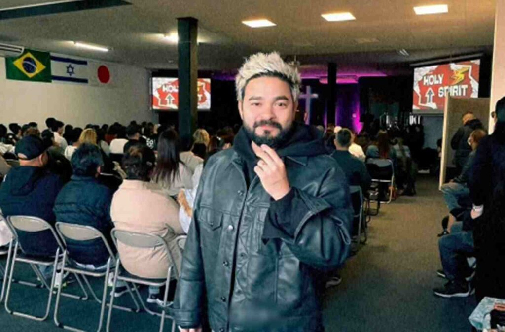 Yudi Tamashiro em igreja durante culto, com fiéis sentados ao fundo