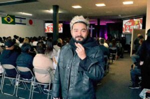 Yudi Tamashiro em igreja durante culto, com fiéis sentados ao fundo