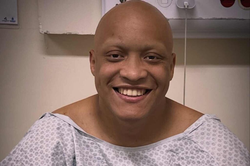 Cantor Jonatha Calixto sorri em quarto hospitalar usando vestimenta médica durante tratamento de saúde.