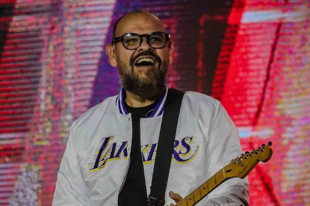 Cantor Marcus Salles toca guitarra durante apresentação em palco com iluminação colorida ao fundo.