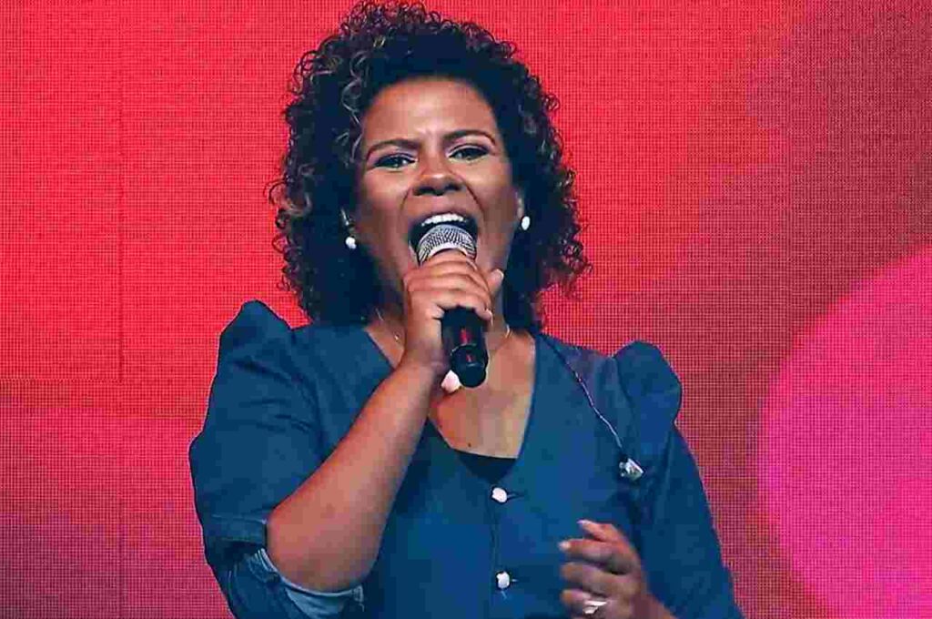 Nívea Soares canta durante apresentação em palco com fundo vermelho iluminado.