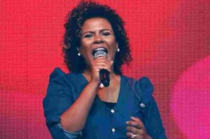 Nívea Soares canta durante apresentação em palco com fundo vermelho iluminado.