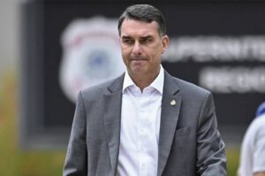 Flávio Bolsonaro caminha usando terno cinza durante evento público.