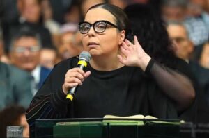 Helena Raquel segurando microfone durante pregação em igreja diante de fiéis.