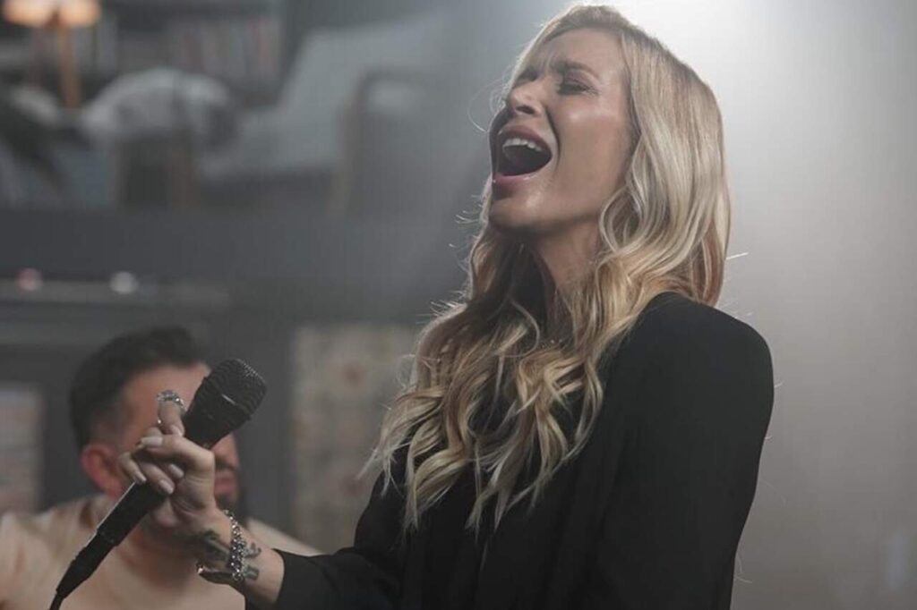 Luíza Possi canta segurando microfone durante apresentação com iluminação suave.