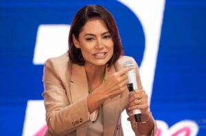 Michelle Bolsonaro fala ao microfone durante evento público, gesticulando enquanto se dirige ao público.