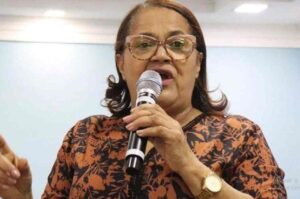 Missionária Cristina Maranhão segura um microfone enquanto ministra mensagem durante culto em igreja evangélica.