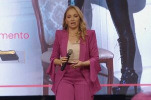 Pastora Patrícia Fernandes ministra palestra em evento cristão, segurando microfone e falando ao público em palco iluminado.