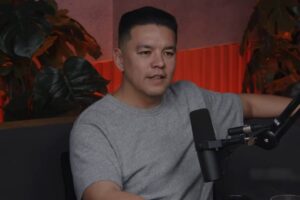 Teo Hayashi durante entrevista em podcast com microfone em estúdio iluminado.