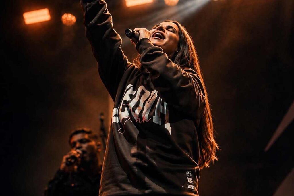 A cantora Aline Barros se apresenta em um palco, segurando um microfone e levantando um dos braços durante um momento de louvor.