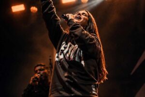 A cantora Aline Barros se apresenta em um palco, segurando um microfone e levantando um dos braços durante um momento de louvor.