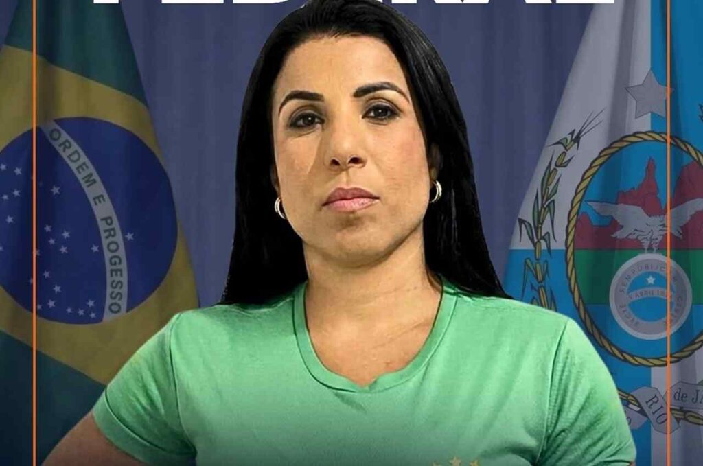 Carla Coltaparece em frente às bandeiras do Brasil e do estado do Rio de Janeiro, usando uma camiseta verde em uma imagem de divulgação.
