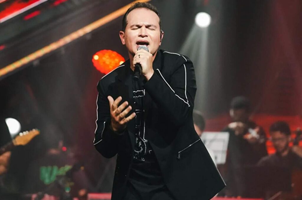 Davi Sacer canta durante apresentação ao vivo em palco iluminado, segurando um microfone e interpretando uma canção de adoração.