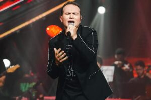 Davi Sacer canta durante apresentação ao vivo em palco iluminado, segurando um microfone e interpretando uma canção de adoração.