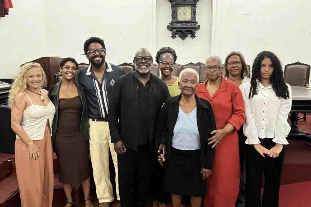 Kleber Lucas posa ao lado de familiares e amigos em um salão histórico após cerimônia, reunindo diferentes gerações para uma foto em grupo.