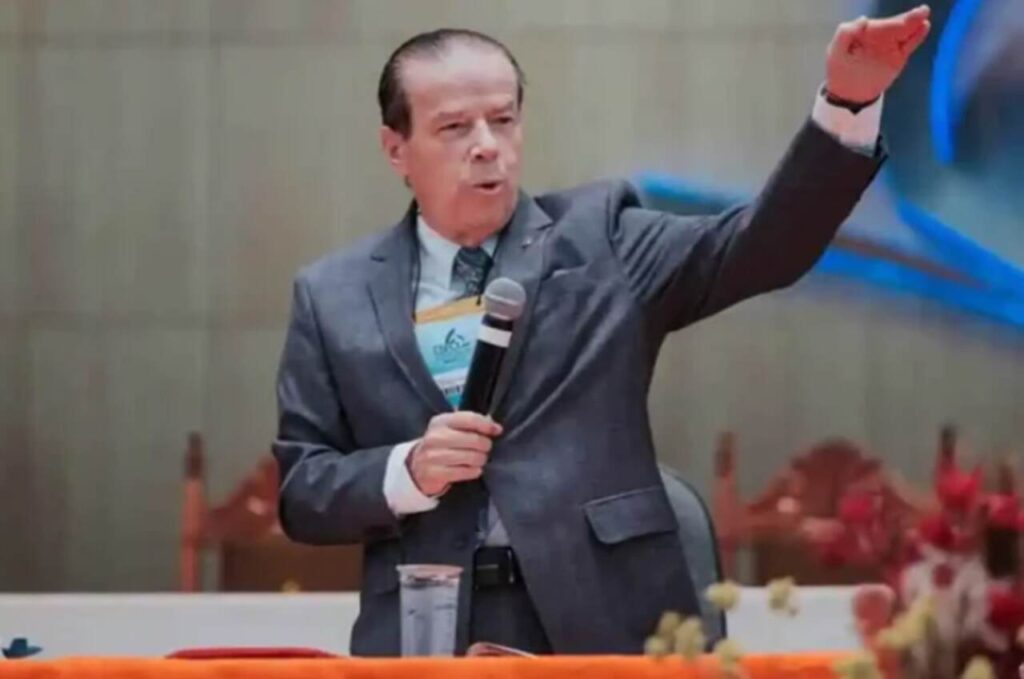 O pastor Elias Cardoso ministra segurando um microfone e gesticulando durante uma conferência em uma igreja.