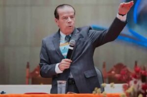 O pastor Elias Cardoso ministra segurando um microfone e gesticulando durante uma conferência em uma igreja.