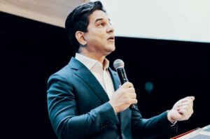 Pastor Jairo Manhães ministra mensagem segurando um microfone durante evento cristão realizado em auditório.