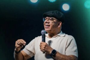 Pastor Josué Gonçalves segura um microfone enquanto ministra em evento cristão diante de uma plateia.