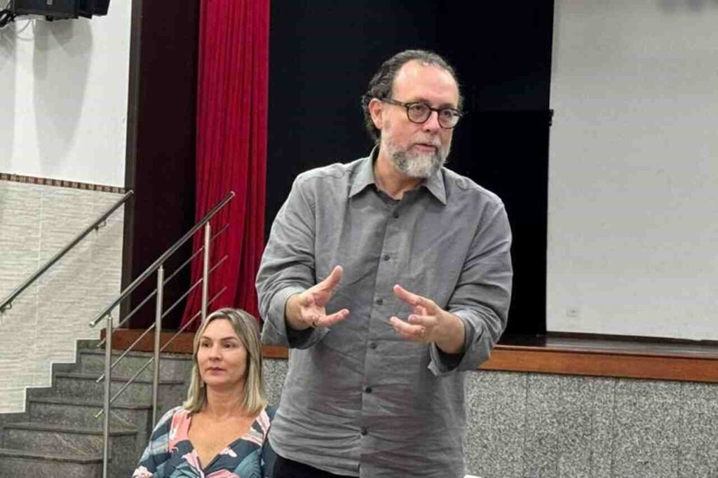 Carlos Bezerra Jr. fala para o público durante encontro realizado em auditório, gesticulando enquanto apresenta uma reflexão.