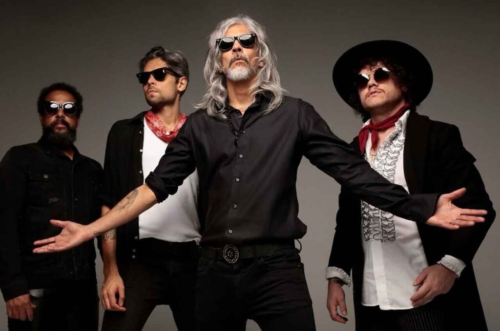 Integrantes da banda Katsbarnea posam para foto promocional usando roupas em estilo rock, óculos escuros e acessórios característicos.