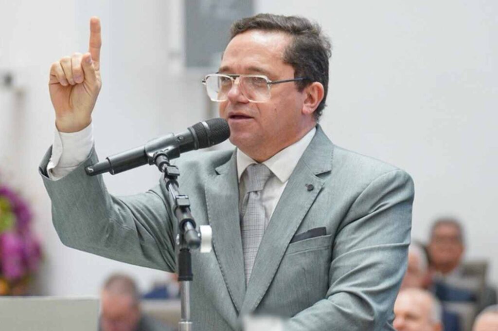 Pastor Waldemir Farias prega ao microfone durante culto, com a mão levantada e o dedo indicador apontado para cima.